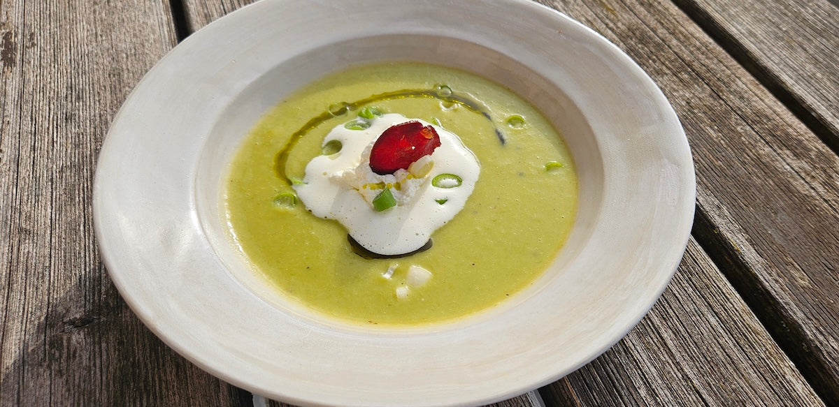 Grüne Lauchsuppe, garniert mit Frühlingszwiebel und Sahne in weißem Suppenteller auf Holztisch
